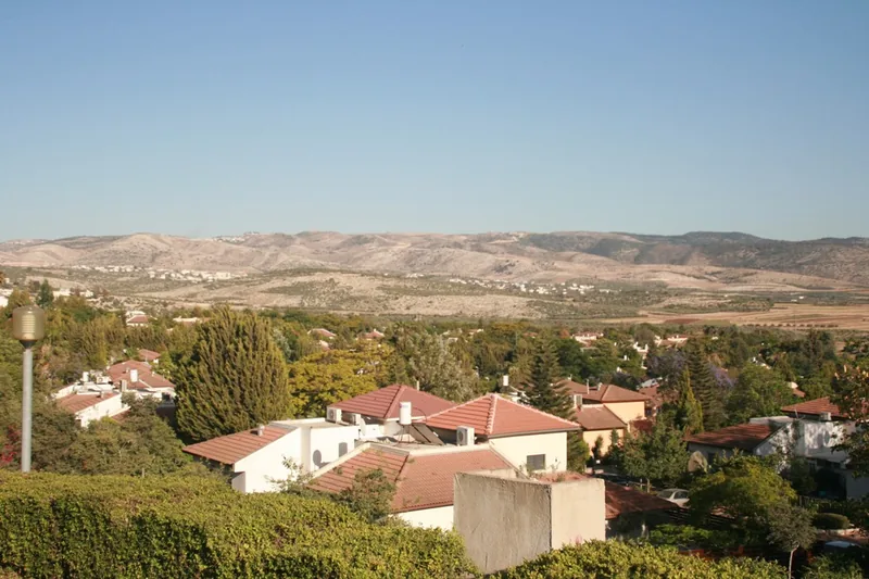 Red-roofed houses of Maccabim among trees, with hills behind